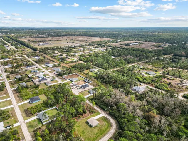 Aerial perspective of a residential lot featuring expansive cleared acreage, mature native vegetation, and unpaved roadway access