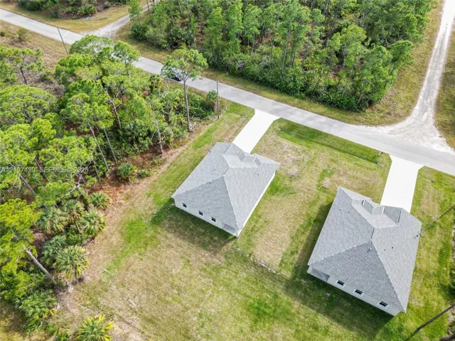 Aerial perspective featuring residential structures with hip roofs, concrete driveways, and expansive cleared grounds bordered by native woodland