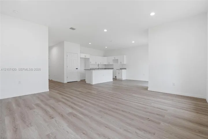 Open-concept space featuring wood-finish flooring, recessed lighting, and white cabinetry, complemented by a kitchen island and neutral stone-finish countertops