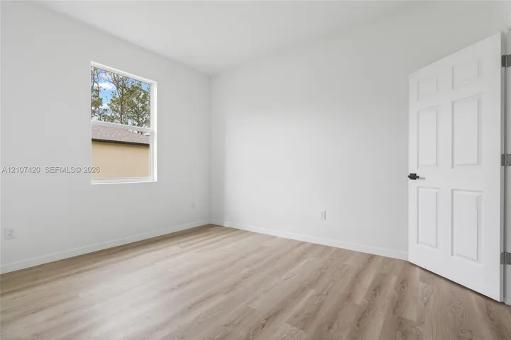 Neutral interior featuring wood-finish flooring, a single-hung window, and a six-panel door with matte black hardware