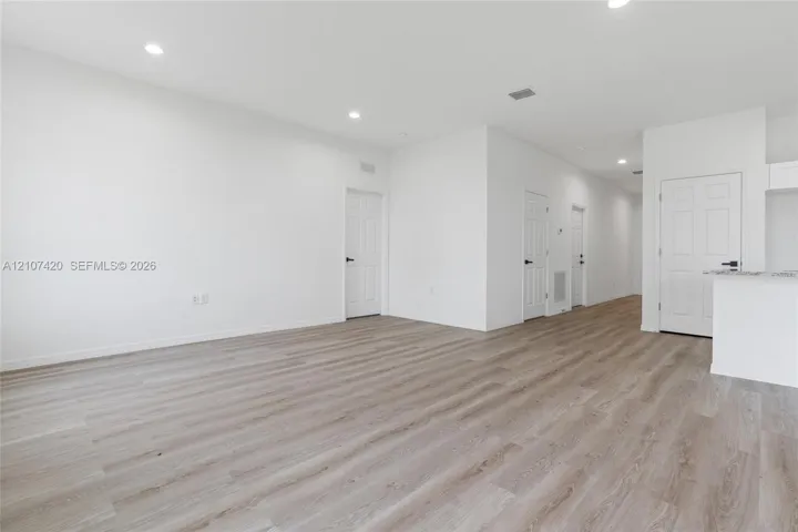 Wood-finish flooring, recessed lighting, white interior doors with matte black hardware, and a stone-surface breakfast bar