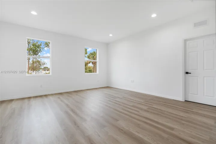 Interior space featuring wood-finish flooring, recessed lighting, dual windows, and a six-panel door with matte black hardware