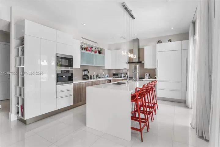 Contemporary kitchen featuring high-gloss cabinetry, a central island with integrated stone countertop, stainless steel built-in appliances, recessed lighting, and large-format tile flooring