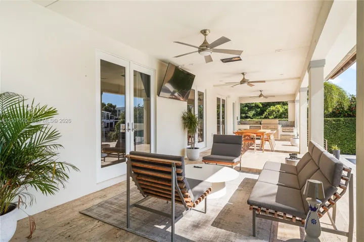 Covered outdoor living area featuring stone-finish flooring, ceiling fans, recessed lighting, and a built-in outdoor kitchen with stone masonry