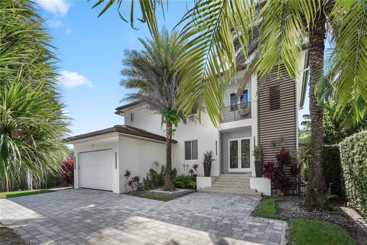 Two-story exterior featuring light-toned stucco, horizontal wood-slat accents, a paver driveway, an attached garage, and a covered front entry with stone-clad stairs
