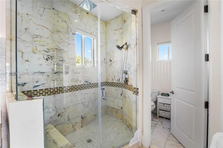 Walk-in shower featuring floor-to-ceiling stone tile surrounds, decorative mosaic tile inlay, built-in stone bench, glass enclosure, and a ceiling-mounted rainfall showerhead