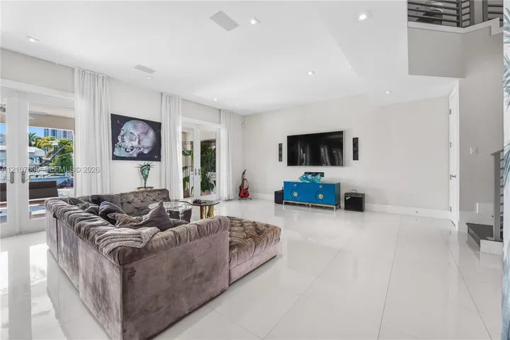 High-ceiling living area featuring large-format polished tile flooring, recessed lighting, and dual sets of glass-paneled double doors