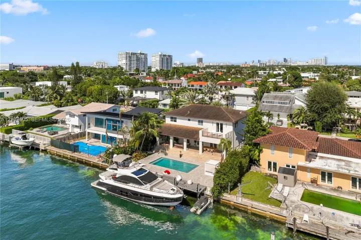 Waterfront two-story residence featuring a private boat dock, rectangular swimming pool, paved patio, and a second-level balcony