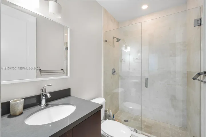 Bathroom featuring a stone-topped vanity with an undermount sink, a glass-enclosed shower with tile surround, and wall-mounted hardware