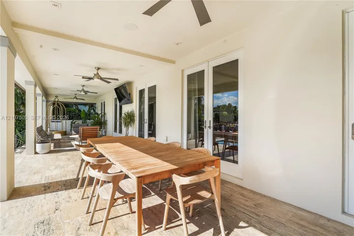 Covered outdoor patio featuring stone-finish flooring, ceiling-mounted fans, recessed lighting, and glass-paneled double doors