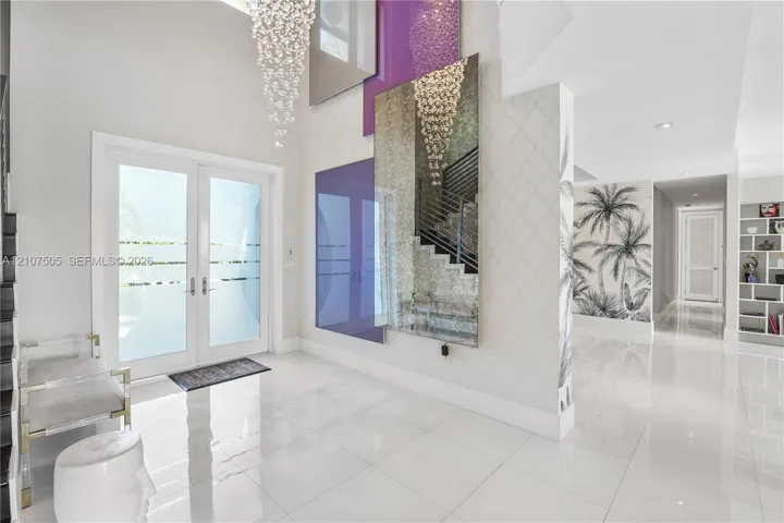 Double-height entryway featuring large-format polished tile flooring, double glass-paneled doors with horizontal frosted accents, a grand tiered crystal chandelier, and custom floor-to-ceiling mirror and glass wall installations