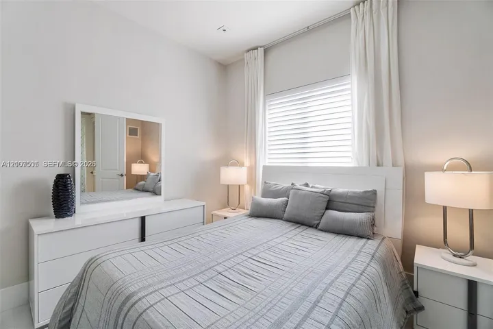 Bedroom interior featuring neutral wall paint, white trim, horizontal blinds, and ceiling-mounted curtain tracks