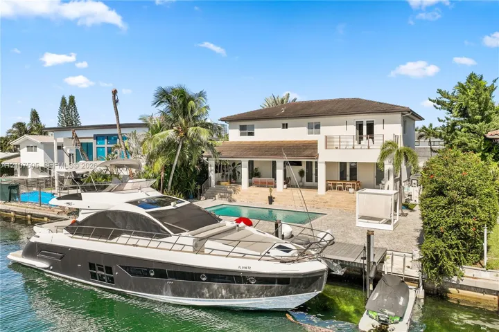 Waterfront property featuring a private boat dock, in-ground swimming pool, stone-paved patio, and two-story exterior with a second-level balcony