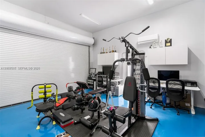 Epoxy flooring, white wall-mounted cabinetry, integrated wall-mounted climate control unit, and industrial-style roll-up garage door