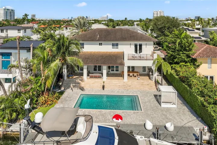 Two-story residence featuring a ground-level covered patio, second-story balcony with metal railings, rectangular swimming pool, stone-paver pool deck, and deep-water dock