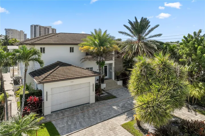 Two-story exterior featuring a light-colored stucco facade, dark tile roof, attached garage, and a paved stone driveway