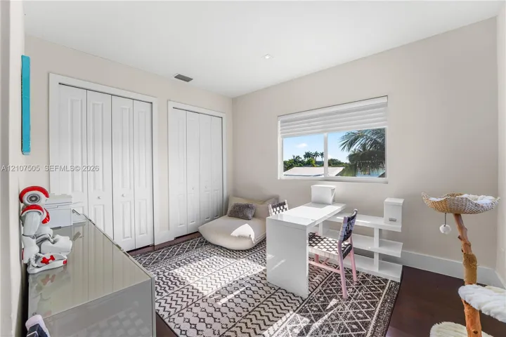 Neutral-toned room featuring dark wood-finish flooring, dual bi-fold door closets, recessed lighting, and a single-pane window with a roller shade