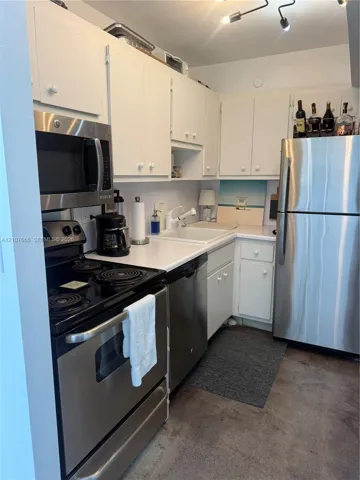 Kitchen featuring stainless steel appliances, white cabinetry, solid-surface countertops, dual-basin sink, and multi-directional track lighting