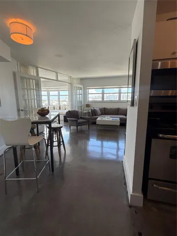 Open-concept floor plan featuring polished concrete flooring, multi-pane French doors, expansive windows with exterior scenery, and integrated stainless steel kitchen appliances