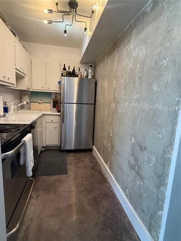 Exposed concrete wall accent, stainless steel refrigerator, white cabinetry, and multi-arm chandelier lighting