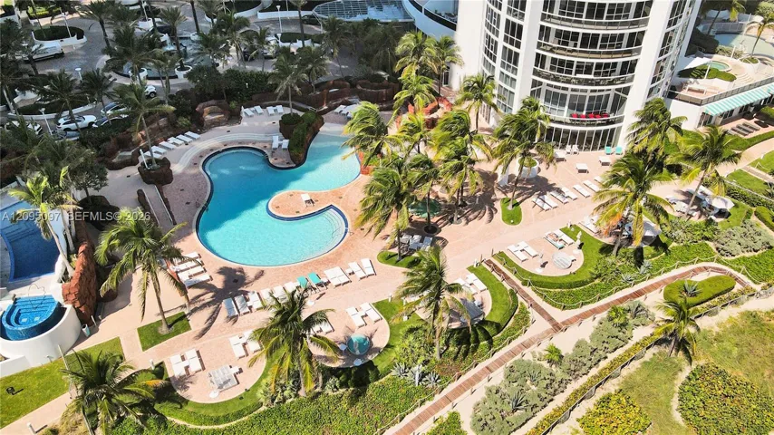 Aerial view of a high-rise building featuring a free-form swimming pool, integrated spa, paved sun deck, and tropical landscaping