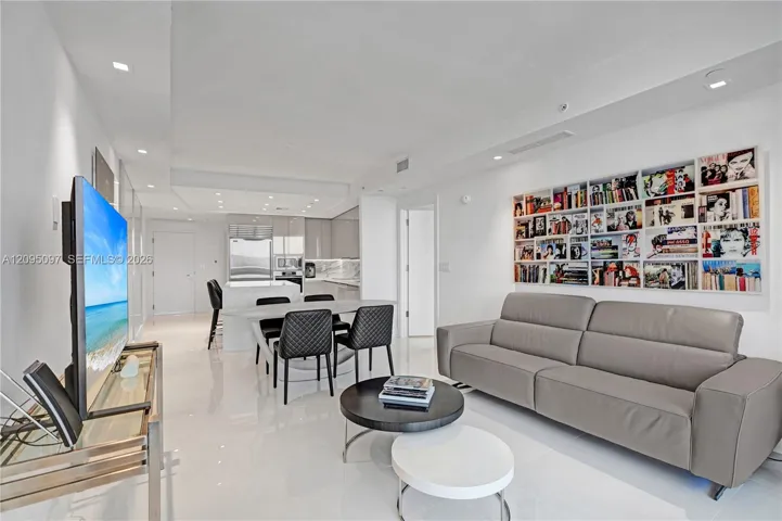 Open-concept interior featuring high-gloss flooring, recessed lighting, a built-in recessed shelving unit, and a kitchen equipped with stone-surfaced countertops and stainless steel appliances