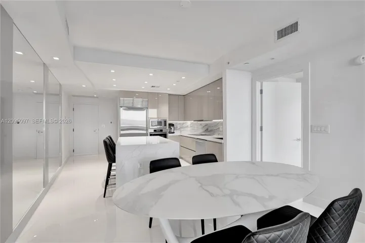 Contemporary kitchen featuring high-gloss cabinetry, stone-surface island, integrated stainless steel appliances, recessed lighting, and polished stone-finish flooring