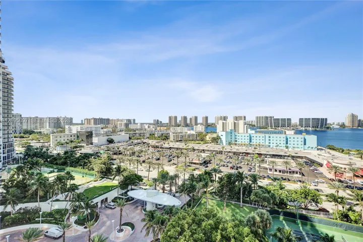Elevated exterior perspective featuring a circular porte-cochère, paved motor court, mature landscaping, and tennis courts