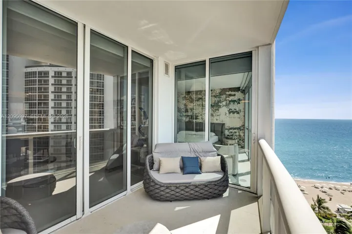 Private balcony featuring expansive floor-to-ceiling glass sliding doors, neutral-toned concrete flooring, and a sleek glass-panel railing, set against a direct ocean backdrop