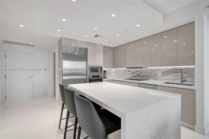 Contemporary kitchen featuring high-gloss cabinetry, a waterfall-edge quartz island, under-cabinet lighting, integrated stainless steel appliances, and stone-finish backsplash