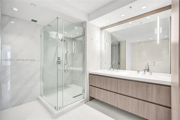 Floating vanity with dual rectangular sinks, frameless glass-enclosed shower, large-format wall tiling, recessed lighting, and integrated wall mirror