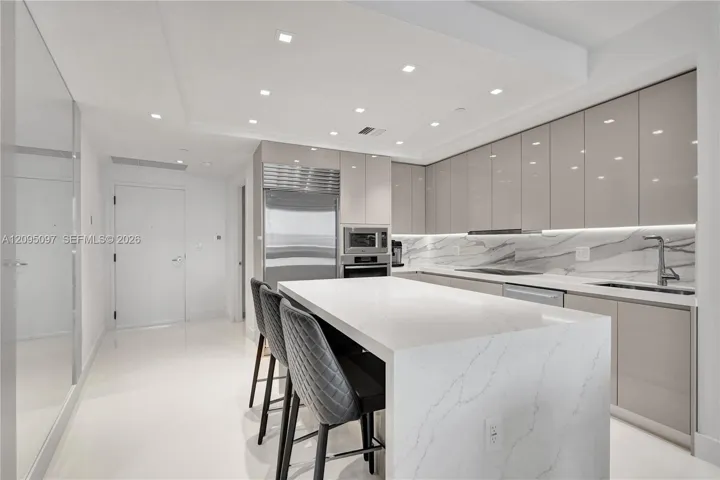 Kitchen featuring high-gloss cabinetry, stone countertops with waterfall edge island, integrated stainless steel appliances, and recessed ceiling lighting