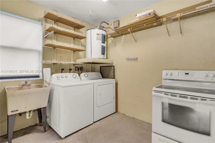 Utility room featuring washer and dryer, a utility sink, wall-mounted shelving, water heater (Stove Range/Oven is no longer there)