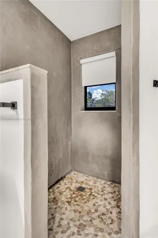 Shower enclosure featuring cement-finish walls, a river rock stone floor, recessed window, and matte black hardware