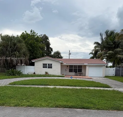 Single-story residence featuring a terracotta-tiled roof, textured stucco facade, attached garage, paved circular driveway, and white vinyl perimeter fencing