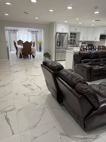 Large-format white tile flooring with grey veining, recessed lighting, white cabinetry, and stainless-steel appliances