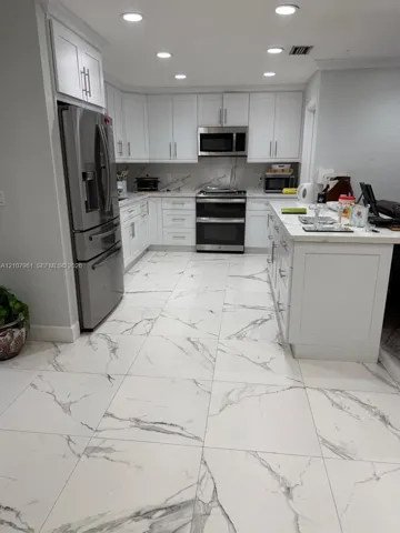 Kitchen featuring white shaker-style cabinetry, stainless steel appliances, a central island with a stone-finish countertop, and large-format tile flooring with a veined pattern