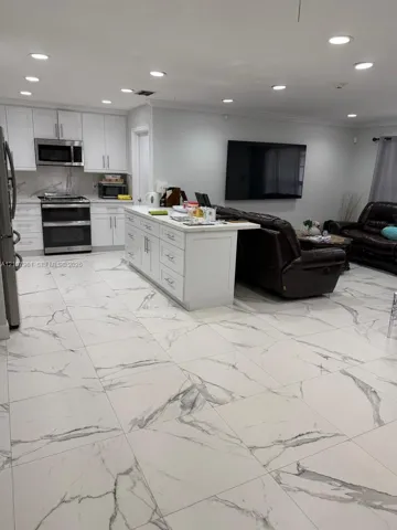Open-concept kitchen featuring white shaker-style cabinetry, stainless steel appliances, a central island, and large-format tile flooring with stone-pattern veining, finished with recessed lighting