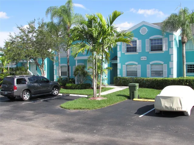 Multi-story exterior featuring a vibrant turquoise facade, white trim detailing, palm tree landscaping, and assigned surface parking