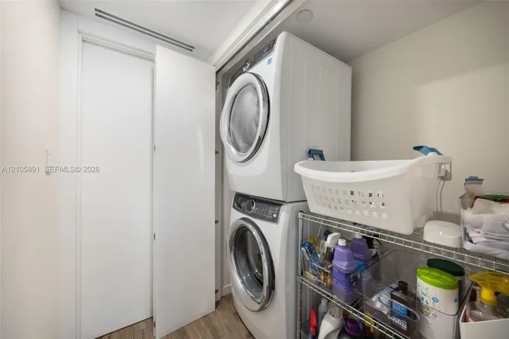 Laundry closet featuring a stacked washer and dryer unit, flat-panel door, and wood-finish flooring