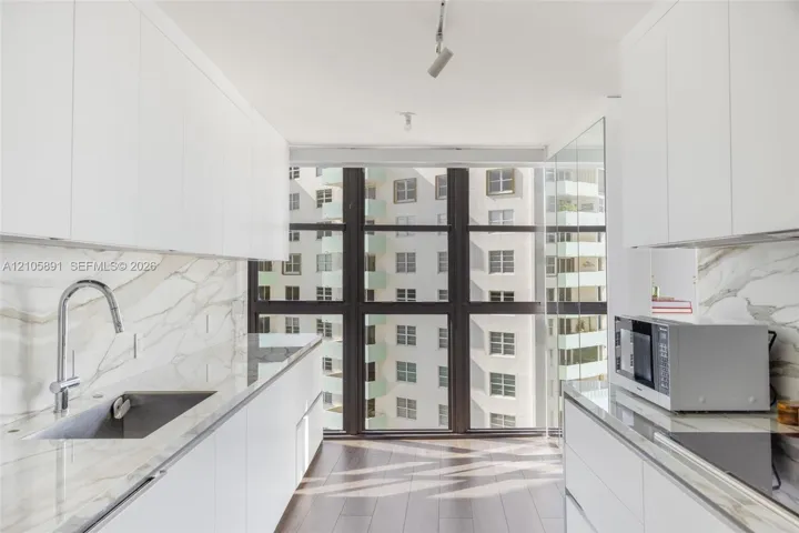 Kitchen featuring white flat-panel cabinetry, floor-to-ceiling windows, veined stone-finish countertops and backsplash, wood-finish flooring, and a stainless steel undermount sink with a gooseneck faucet