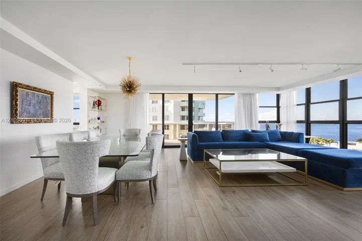 Open-concept interior featuring wood-finish flooring, floor-to-ceiling windows with water vistas, built-in recessed display shelving, and modern track lighting