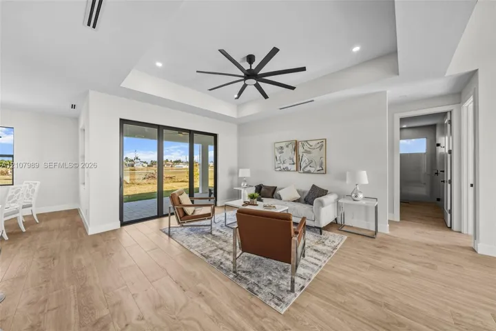 Tray ceiling featuring a multi-blade ceiling fan, wood-finish flooring, recessed lighting, and expansive multi-panel sliding glass doors