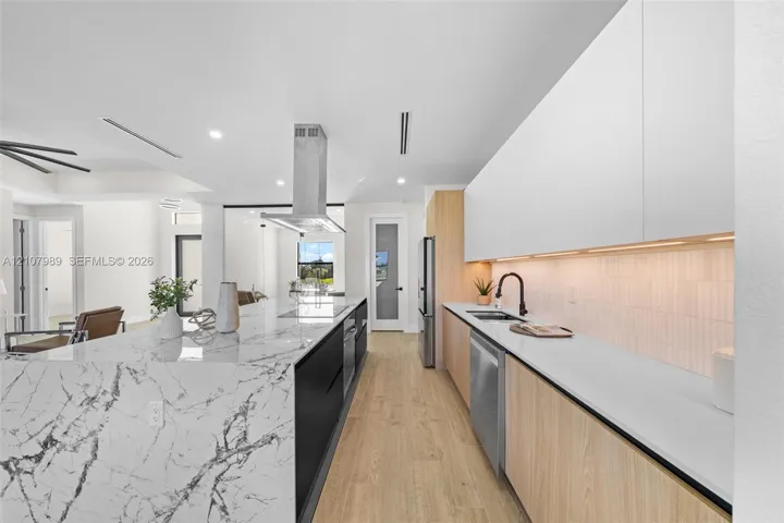 Modern kitchen featuring a waterfall-edge stone island, wood-finish cabinetry, white slab-front upper cabinets, stainless steel range hood, and integrated under-cabinet lighting