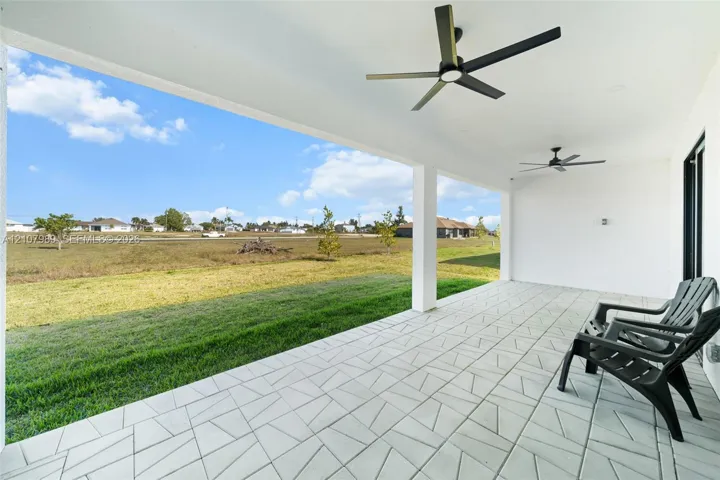 Covered patio featuring patterned concrete tile flooring, dual ceiling fans, and structural support columns overlooking an open grass lawn