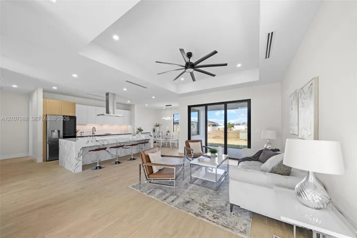Tray ceiling with multi-blade ceiling fan, expansive kitchen island with stone-finish waterfall countertop, wood-finish flooring, and multi-panel sliding glass doors
