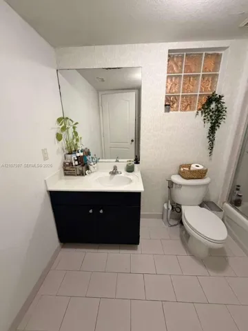 Bathroom featuring a vanity with a white countertop and integrated sink, a large wall-mounted mirror, glass block window accent, and neutral tile flooring