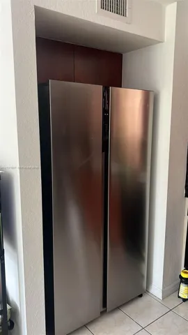 Stainless steel side-by-side refrigerator recessed into a custom built-in nook featuring dark wood-finish cabinetry