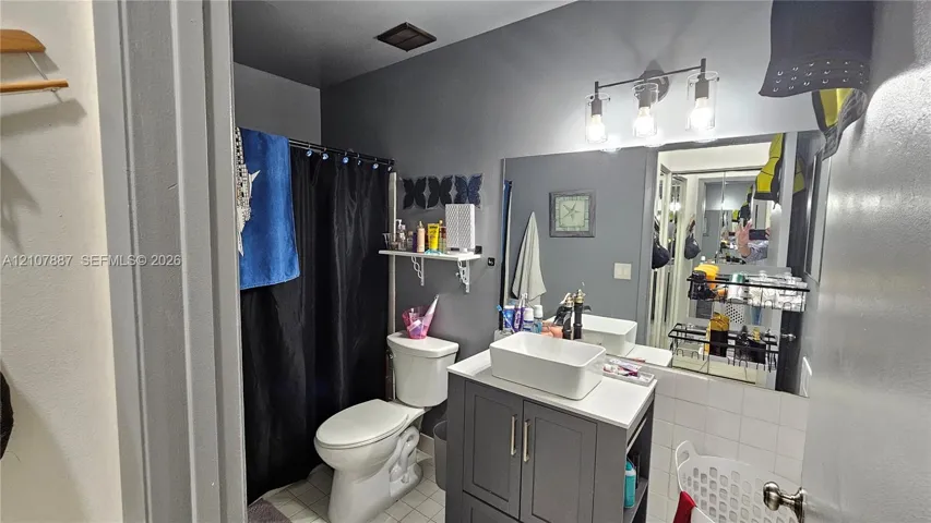 Bathroom featuring a vanity with a white rectangular vessel sink, solid-surface countertop, three-light fixture, and large wall-mounted mirror