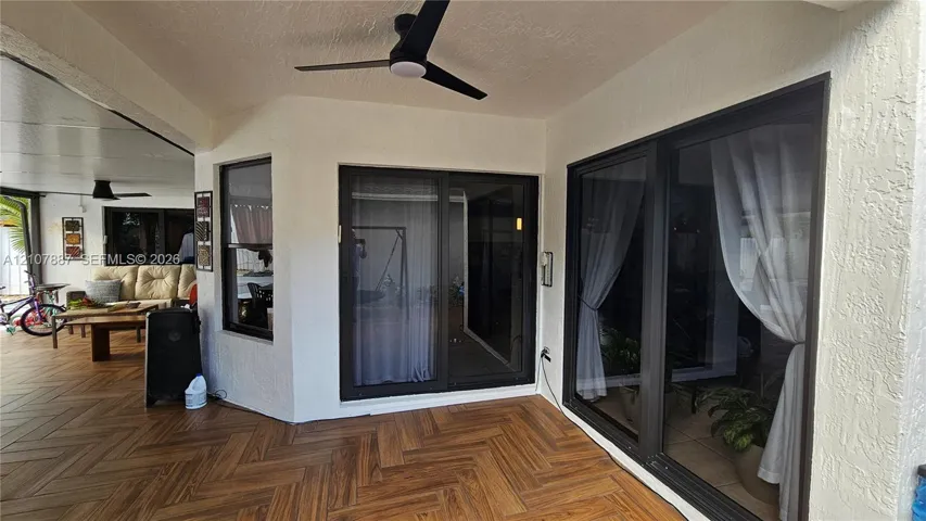 Covered patio featuring herringbone-patterned flooring, dark-framed sliding glass doors, and a ceiling-mounted fan